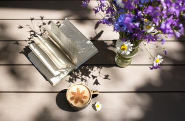 Good morning, romantic atmosphere, comfort, tranquility, relaxation at home. a cup of coffee with milk, a vase with wild lilac flowers, an open book on a wooden table. Nobody