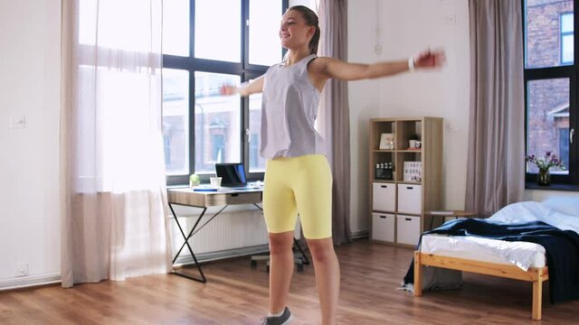 sport, fitness and healthy lifestyle concept - smiling teenage girl with smart watch doing jumping jack or star jump exercise at home