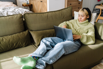 Asian girl working with laptop while resting on sofa