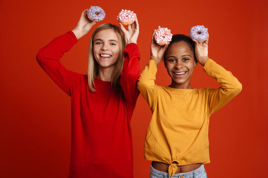 Multiracial two girls laughing while making fun with donuts