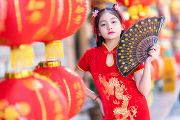 little Asian girl wearing red traditional Chinese cheongsam and holding a Fanningand lanterns with...