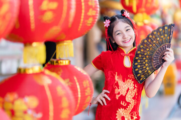little Asian girl wearing red traditional Chinese cheongsam and holding a Fanningand lanterns with...