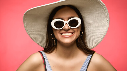 Smiling brunette woman in sunglasses and swimsuit posing isolated on pink.