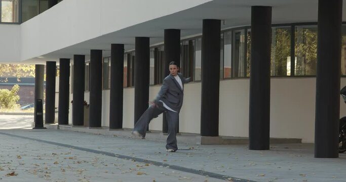 Attractive businesswoman in formal grey suit is dancing outside the office, financial district, modern constructivist building with columns on background. The concept of urban city scene