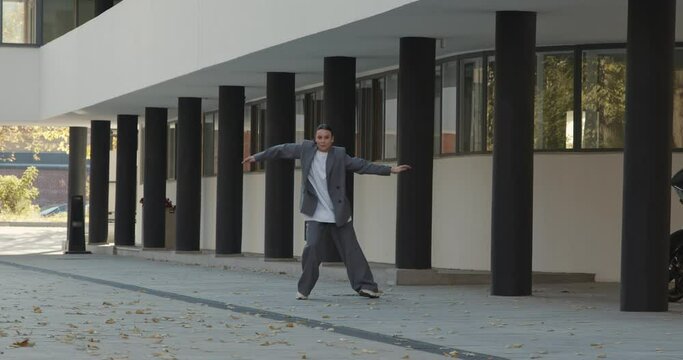 Attractive businesswoman in formal grey suit is dancing outside the office, financial district, modern constructivist building with columns on background. The concept of urban city scene