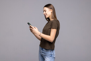 Portrait of an attractive young woman standing with a mobile phone against a grey wall