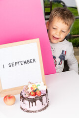 adorable happy cheerful boy in glasses show letter board with text 1 September, festive cake with ABC. Knowledge day. Concept of education, back to school. Selective focus