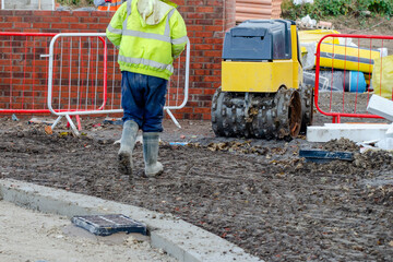 Construction worker operating remote controlled trench compactor to compact ground around new build residential house - obrazy, fototapety, plakaty