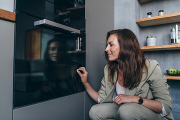 Woman looks into the oven through the glass at the food being cooked