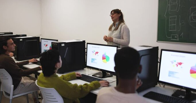 Mature teacher working with students inside computer classroom at school
