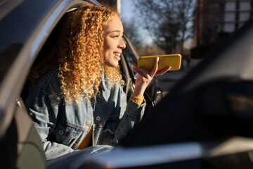 Hispanic curly haired woman getting out of car with smartphone at sunset
