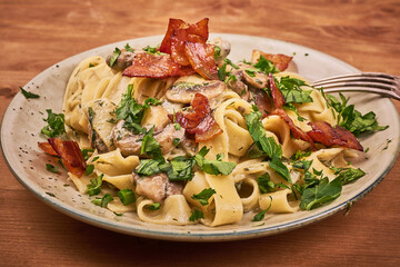 Portion of fettuccine pasta with creamy mushroom sauce and fried pancetta on a plate - classic Italian pasta