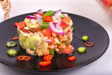 Restaurant serving of panzanella salad on a black plate, garnished with chili rings