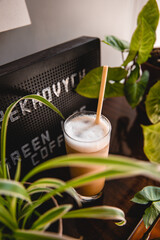 Coffee in a glass with cream or milk, on a beautiful wooden background of a bar with green plants in a cafe. Great image for a banner or menu