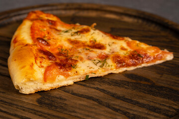 A piece of delicious pizza on a wooden oak board. Top view of a delicious freshly baked hot pizza