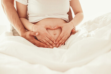 Fototapeta na wymiar Crop anonymous pregnant couple cuddling on cozy bed in morning