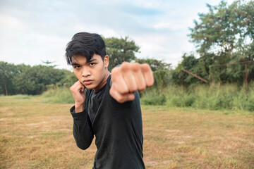 A serious young man in a dark gray sweatshirt doing shadow boxing outside a field. Throwing a right...