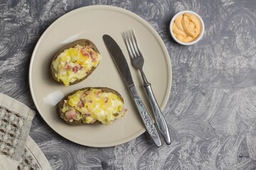 Potatoes with cheese filling and sauce in a bowl on a plate with a fork and a knife on a gray background