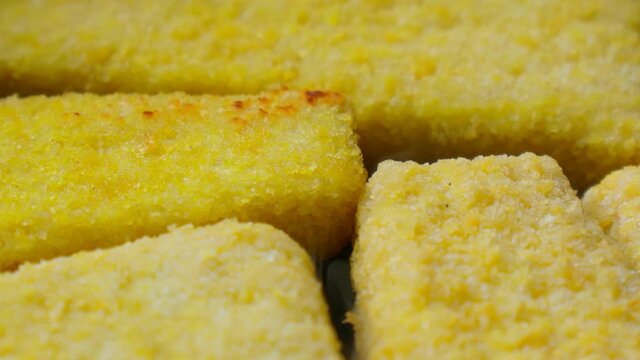 Grilled fish cutlets in the shape of a triangle breaded in a pan closeup. Nuggets for quick cooking