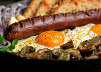 Fried eggs and sausage with mushrooms served in cast iron pan in the kitchen