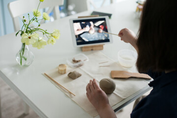 woman watching an online masterclass and sculpting a small pumpkin out of clay with tools - DIY and hobby project