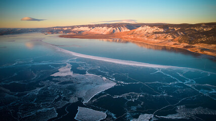View of the frozen Lake Baikal from the air. Transparent ice with cracks. Mountain landscape. 