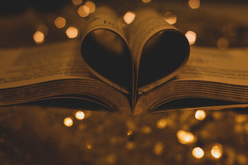 Heart shaped book pages on shiny golden bokeh background