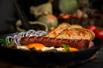 Sausage and fried eggs with toasted bread, mushrooms and onions served in cast iron dish. Selective focus on the sausage