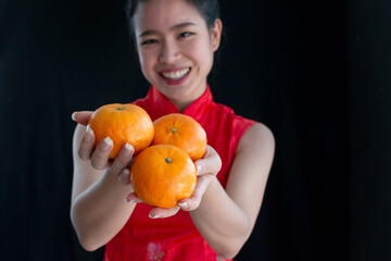 Smiling young woman in Chinese traditional dress, holding or giving oranges is a symbol of wealth...