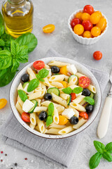 Healthy pasta salad with tomatoes, cucumbers, red onions, olives and cheese in a bowl on a gray background. Copy space.
