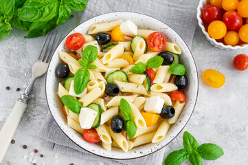 Healthy pasta salad with tomatoes, cucumbers, red onions, olives and cheese in a bowl on a gray background. Copy space.