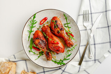 Delicious baked chicken drumsticks or legs with paprica, chili pepper, arugula and thyme on white background. Top view, flat lay