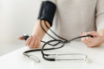 Woman measuring blood pressure by herself at home with manual device. Self care and medical concept.