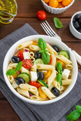 Healthy pasta salad with tomatoes, cucumbers, red onions, olives and cheese in a bowl on a dark wooden background. Copy space.