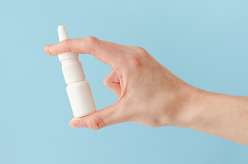 Female hand holding nasal spray on blue background. Seasonal allergy and common cold concept.