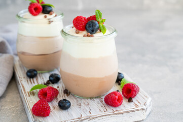 Dessert three chocolate in a glass jar with fresh blueberries, raspberries and blackberries on top on a gray concrete background. Dessert with three layers of different taste. Copy space.