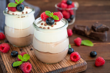 Dessert three chocolate in a glass jar with fresh blueberries, raspberries and blackberries on top on a dark wooden background. Dessert with three layers of different taste. Copy space.