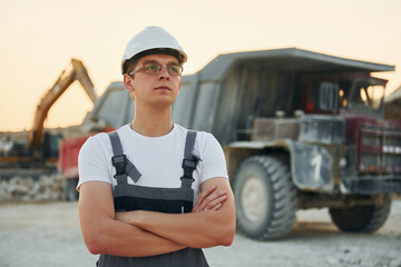 Fototapeta premium Near loading vehicle. Worker in professional uniform is on the borrow pit at daytime
