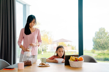 Obraz na płótnie Canvas Asian girl using tablet computer while having breakfast with her mother