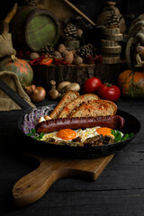 Fried eggs and sausage with mushrooms served in cast iron pan in the kitchen