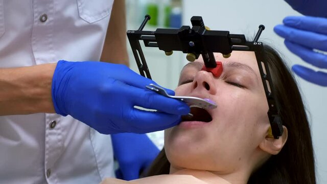 Orthodontist installs dental facebow on woman face, prosthetics. Orthodontic treatment in dentistry, dental prosthetics. Bite and joint, occlusion correction before installing veneers crowns.