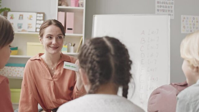 Medium slowmo shot of female speech therapist working with group of children in bright classroom, learning rules of pronunciation together