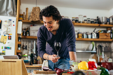 Fototapeta na wymiar man preparing vegetable salad at home while drinking red wine