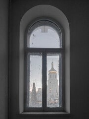 Arched window of an old house, behind which the bell tower of St. Sophia Cathedral and the Christmas tree. Kyiv, Ukraine.