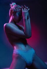 Nude woman in colorful bright neon lights cover breast by hands posing in studio, portrait of...