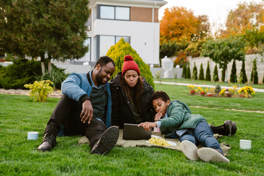 Black family using tablet computer during picnic at backyard