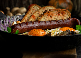 Fried eggs and sausage with mushrooms served in cast iron pan in the kitchen