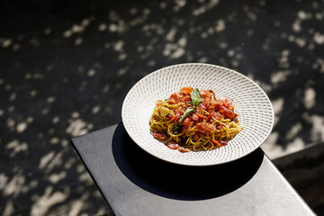 Spaghetti dish on black iron table with tree shadow bokeh