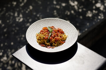 Dried chili and bacon spaghetti dish on black iron table with tree shadow bokeh