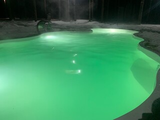 Thermae - a heated outdoor pool illuminated in green at night in the snow with steam coming from the pool in winter